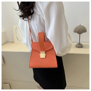 Detail of orange crocodile texture handbag with gold buckle worn as crossbody bag