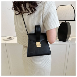 Side view of black crocodile pattern handbag with gold clasp on a female model