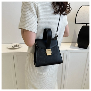 Detail of black crocodile pattern handbag with golden metal square buckle and strap