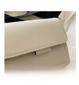 Detalle de bolso cuadrado de piel crema con costuras precisas y correa de hombro tejida