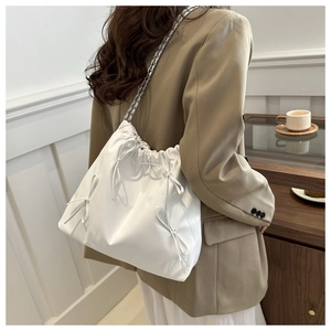 Detail of white drawstring shoulder bag with bow decor and silver chain strap