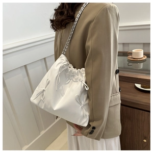 Detail of white drawstring bucket bag with decorative bows and metal chain strap