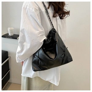 Détail du sac seau noir à cordon avec nœud décoratif et bandoulière en chaîne métal