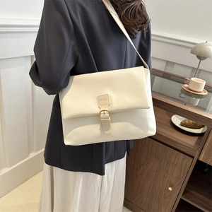 Chic creamy white leather shoulder bag with gold hardware shown on a model in a cozy room