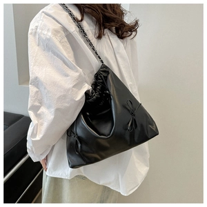 Detail of a black leather drawstring bucket bag with side bow and chain strap