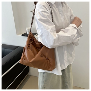Détail d'un sac marron avec plis à cordon, chaîne métallique et nœuds décoratifs