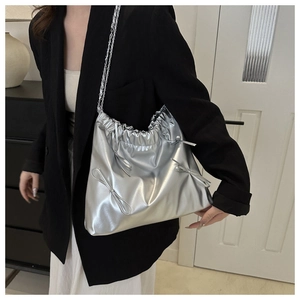 Close-up of silver metallic bucket bag with bow details and chain strap shown on model
