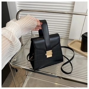 Detail of black faux leather handbag featuring crocodile pattern and gold square lock