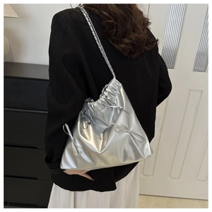 Detail of silver metallic drawstring bucket bag with decorative bows and chain strap