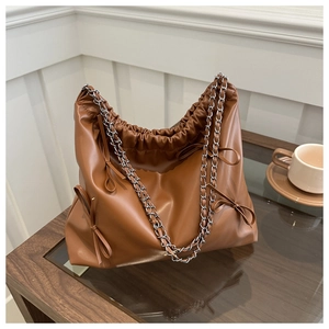 Detail of dark brown pleated bucket bag with bow accents and metal chain strap