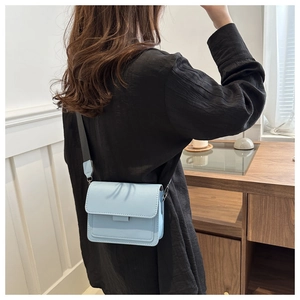 Bolso cuadrado azul claro con correa ancha llevado por una modelo en una sala moderna