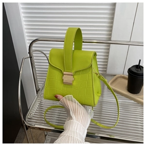 Macro detail of lime green croc-effect texture and metallic lock on a square handbag