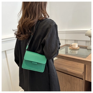 Bolso bandolera cuadrado de cuero verde con correa ancha mostrado por una modelo en casa