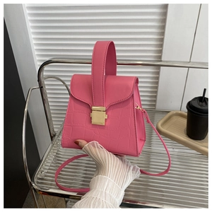 Detail of pink crocodile embossed handbag featuring a gold square lock and shoulder strap
