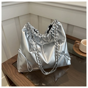Detail of silver metallic bucket bag with drawstring closure and bow accents on a table
