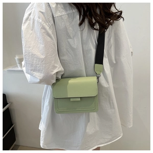 Detalle de bolso bandolera rectangular verde claro con una elegante correa ancha tejida