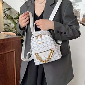 White mini backpack with M-pattern print and gold chain detail on grey blazer
