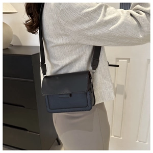 Detalle de un elegante bolso bandolera negro con una correa de tela ancha y ajustable