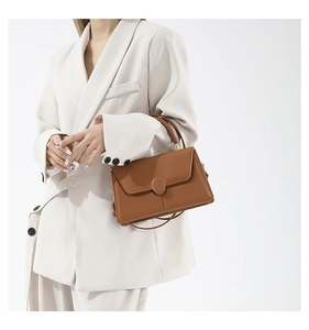 Vue détaillée du sac à main en cuir marron avec boucle en métal sur un blazer beige