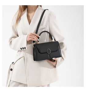 Détail du sac carré en cuir noir montrant le fermoir ovale doré et la bandoulière réglable