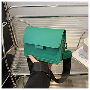 Detalle de bolso bandolera de cuero verde con textura granulada y correa ancha de tela