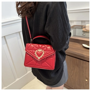 Detail of red quilted crossbody bag featuring a golden crown heart lock and chain strap