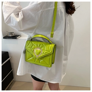 Detailed view of lime green quilted crossbody bag featuring a golden heart crown ornament