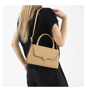 Gros plan d'un sac à main beige structuré avec un fermoir doré ovale sur tenue noire