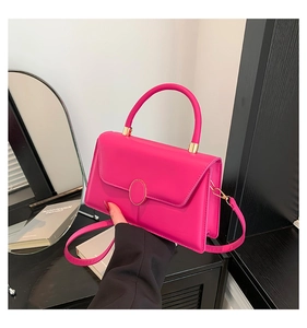 Detail view of hot pink crossbody bag with gold round clasp on a wooden surface