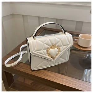 Detailed side view of white quilted crossbody bag with golden heart crown hardware on a table