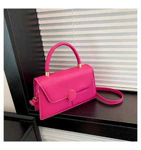 Detail of rose pink square handbag featuring a gold circular lock on black wood sill