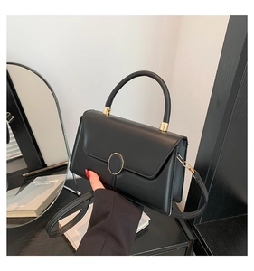 Close-up of black leather handbag with round gold clasp and elegant handle