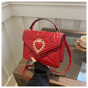 Detail of red quilted PU leather bag with golden crown heart clasp on wooden table