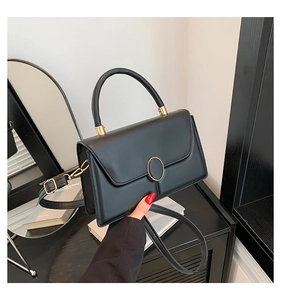 Detail of matte leather texture and oval gold buckle on a black rectangular handbag