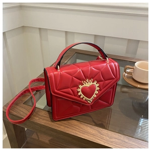 Detail of red quilted crossbody bag with a golden heart crown buckle on a wooden table