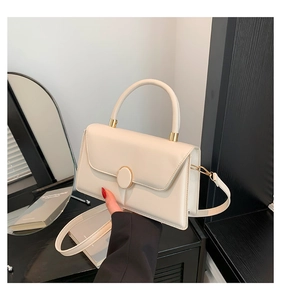 Detail view of cream minimalist crossbody bag with golden round clasp in chic setting