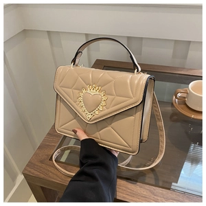 Close-up of beige quilted crossbody bag featuring a golden heart and crown metal buckle