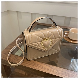 Detail of khaki quilted crossbody bag with golden heart crown buckle on wooden table