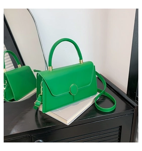 Detail of green minimalist square handbag with metal buckle on a textured cabinet