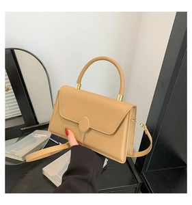 Detail view of beige square handbag with round gold metal buckle and sleek top handle