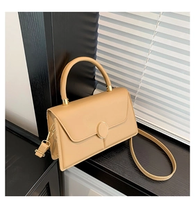 Detail of minimalist beige square handbag with oval metal buckle on a dark wood surface