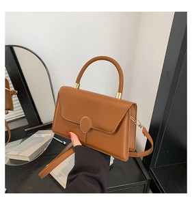 Detail of caramel leather handbag featuring oval metal clasp and elegant stitching