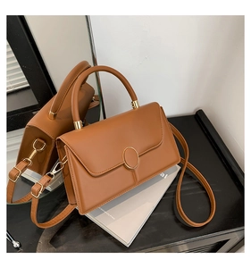 Brown retro leather handbag with a gold oval buckle on a book, showcasing detail and texture