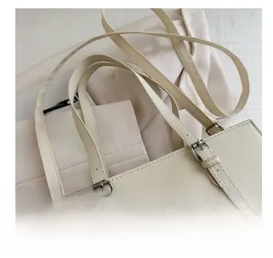 Close-up of beige tote bag showing cross-grain leather texture and silver buckles