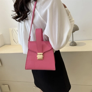 Pink crocodile pattern small square handbag with gold buckle shown on a white tabletop