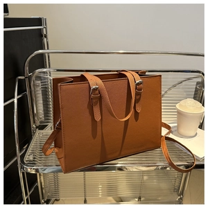 Brown faux leather tote bag with silver buckle details on industrial metal shelf