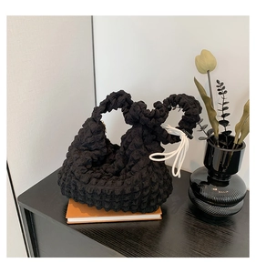 Détail d'un sac seau noir à texture bulle sur un livre orange avec décoration