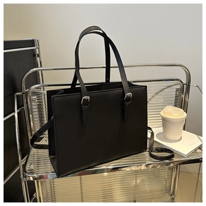 Detail of minimalist black tote bag with silver buckle handles on modern metal shelf