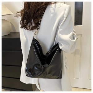 Detail of a large black glossy hobo bag with a gold metal chain strap on a white blazer