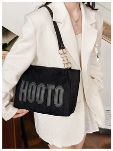 Gros plan du sac cabas noir avec écusson HOOTO et détail de chaîne dorée sur blazer